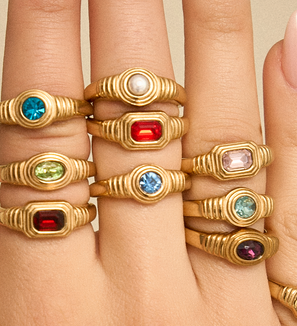 A close-up of a hand wearing multiple gold rings with colourful birthstone gemstones. 