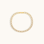 Gold tennis bracelet with cubic zirconia stones on a light beige background