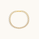 Gold tennis bracelet with cubic zirconia stones on a light beige background