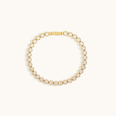 Gold tennis bracelet with cubic zirconia stones on a light beige background